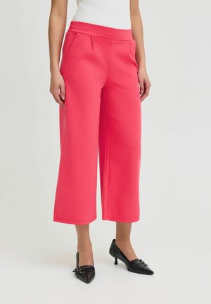 Roze wijde broek met een zachte textuur, met een relaxte pasvorm en twee zijzakken. Gdraagd met zwarte hakken.
