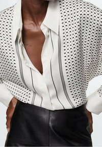 White button-up shirt featuring a geometric black pattern, vertical stripes, and a relaxed fit, accompanied by a leather skirt.