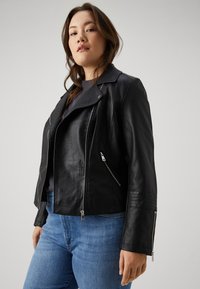 Black leather jacket with a notched collar, zippered pockets, and textured detailing on the sleeves, paired with blue jeans.