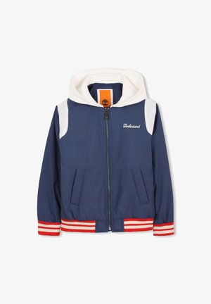 Marineblauwe bomberjack met een witte capuchon, rood-wit gestreepte boorden, ritssluiting aan de voorkant en twee zijzakken; voorzien van Timberland-logo.