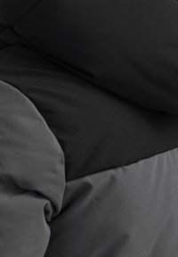 Tessuto imbottito nero e grigio scuro con una texture liscia, caratterizzato da sezioni sovrapposte e piegate e un design elegante e minimal.