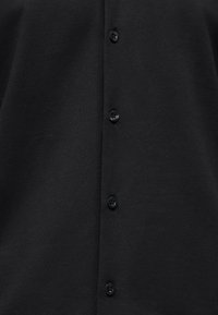 Μαύρο πουκάμισο με κουμπιά, με λεία υφή υφάσματος, έξι στρογγυλά μαύρα πλαστικά κουμπιά στο μπροστινό μέρος και άνετη εφαρμογή.