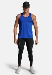 Blaues Sporttanktop, schwarze Leggings mit strukturiertem Detail und weiße Sneakers. Das Tanktop hat einen Rundhalsausschnitt und eine taillierte Passform.