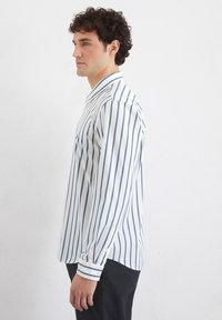 Weißes Langarmhemd mit schmalen marineblauen vertikalen Streifen. Mit klassischem Kragen und Knopfmanschetten. Glatte Stofftextur.