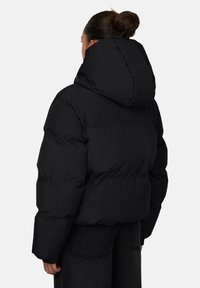 Czarna kurtka puchowa z oversize'owym kapturem, pikowaną fakturą i elastycznymi mankietami. Posiada ściągnięty w talii krój i gładką powierzchnię.