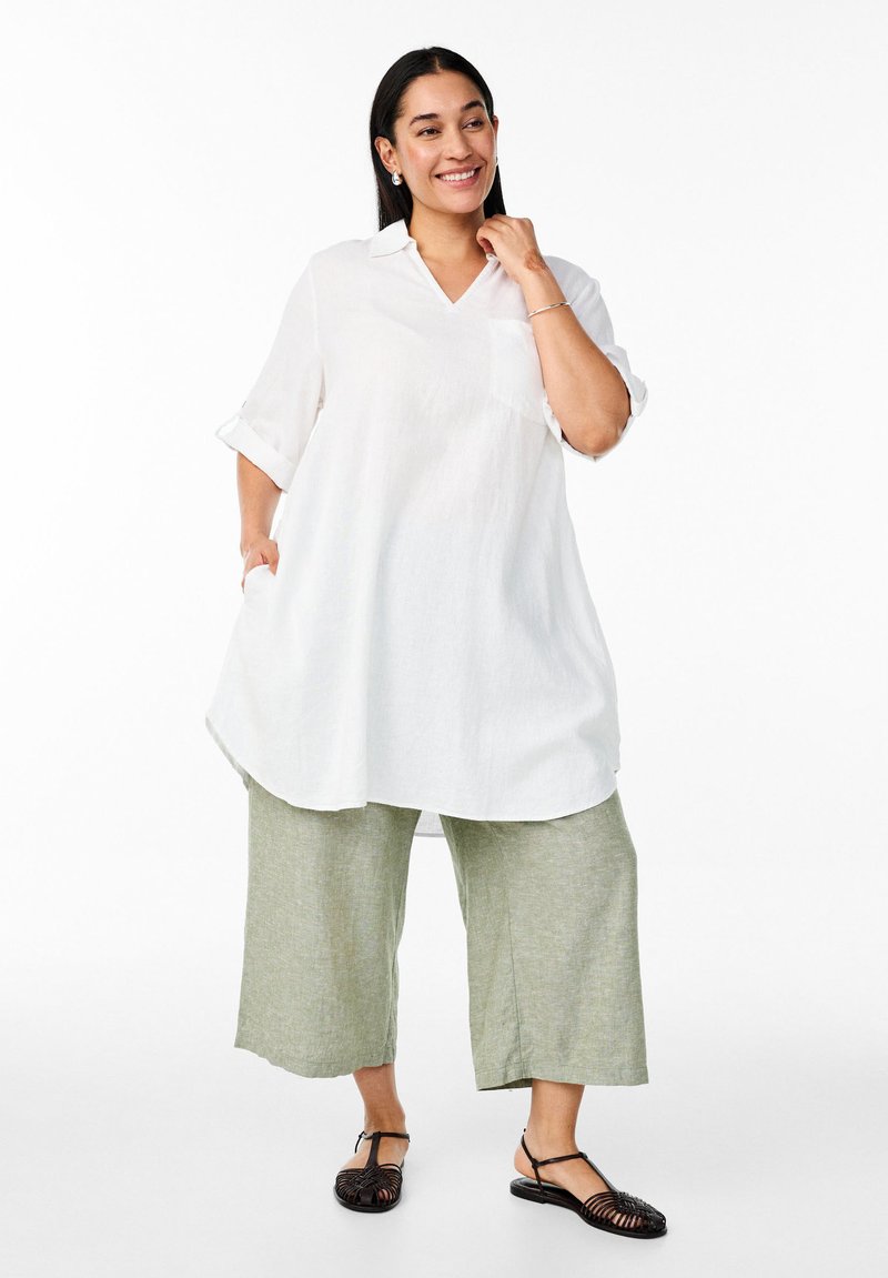 Bela lanena srajca z V-izrezom, zavihki na rokavih in žepom na prsih, v kombinaciji z svetlo zelenimi lanenimi culottes in črnimi sandalmi na trakove.
