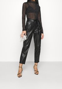 Svart mesh långärmad topp med silvernitar, hög halsringning. Svarta högmidjade läderbyxor, figurnära. Genomskinlig, smyckad handväska. Slingback klackar i svart.