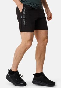 Svarta shorts med texten "SWEDENMOUNT" i reflekterande silver, sidofickor, i kombination med svarta vattentäta skor och ankelsockar.