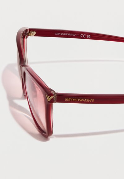 Ορθογώνιο κόκκινο σκελετός γυαλιών Emporio Armani με χρυσό λογότυπο στα πλαϊνά και διαφανείς φακούς, εμφανίζεται σε κλειστή γωνιακή προβολή.