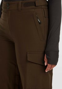 Bruine cargobroek van rekbaar materiaal, met knopen aan de voorkant, een ritszak en een zijcargo pocket met drukknoopsluiting.