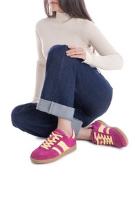 Baskets rose et jaune vives avec un dessus en daim, design à lacets et semelle en caoutchouc, associées à un jeans bleu retroussé et un pull beige.