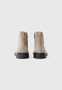 Stivali ankle in suede beige con suola in gomma nera, caratterizzati da una cerniera posteriore e dettaglio del logo impresso sul tallone.