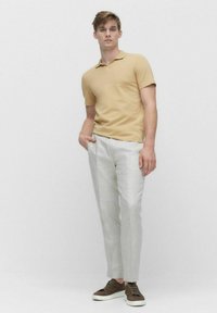 Pikeepaita vaaleassa beigesävyssä, slim fit; vaaleanharmaat housut sileällä pinnalla; tummanruskeat sneakerit valkoisilla pohjilla.