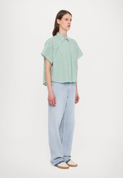 Green and white striped short-sleeve shirt paired with light blue high-waisted jeans, featuring a relaxed fit and slight cuff detail.