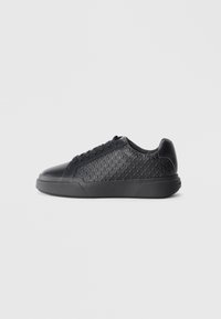 Black sneaker made of textured synthetic material, featuring a diamond pattern, round toe, flat rubber sole, and classic lace-up design.