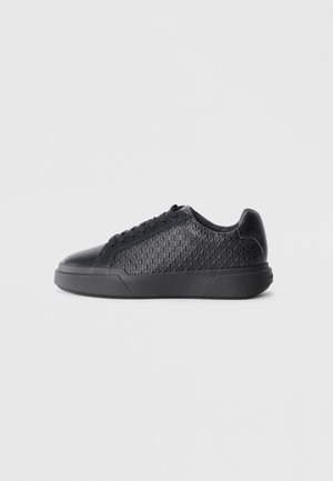 Black sneaker made of textured synthetic material, featuring a diamond pattern, round toe, flat rubber sole, and classic lace-up design.