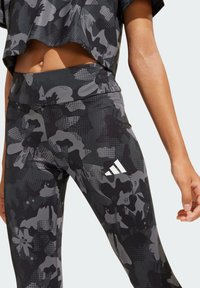 Leggings con un patrón floral en negro y gris, de cintura alta, fabricados con un material elástico; cuentan con un logo blanco cerca de la parte inferior.