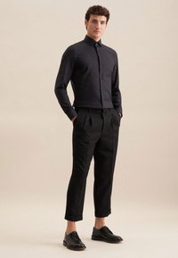 Camicia nera con bottoni, colletto strutturato, taglio slim. Abbinata a pantaloni neri su misura e scarpe nere stringate. Tessuto con una texture liscia.