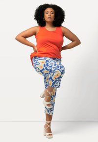 Haut sans manches rouge associé à des leggings bleu à motifs avec des designs floraux jaunes. Sandales à talons hauts blanches avec des brides à la cheville.
