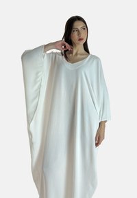 Løs hvid kaftan med brede ærmer, lavet af let, tekstureret stof. Har en v-udskæring og en svajende silhuet.