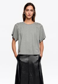 Szara bawełniana koszulka z krótkim rękawem, ozdobiona plisami i metalowymi ćwiekami na ramionach. Połączona z długą czarną skórzaną spódnicą.