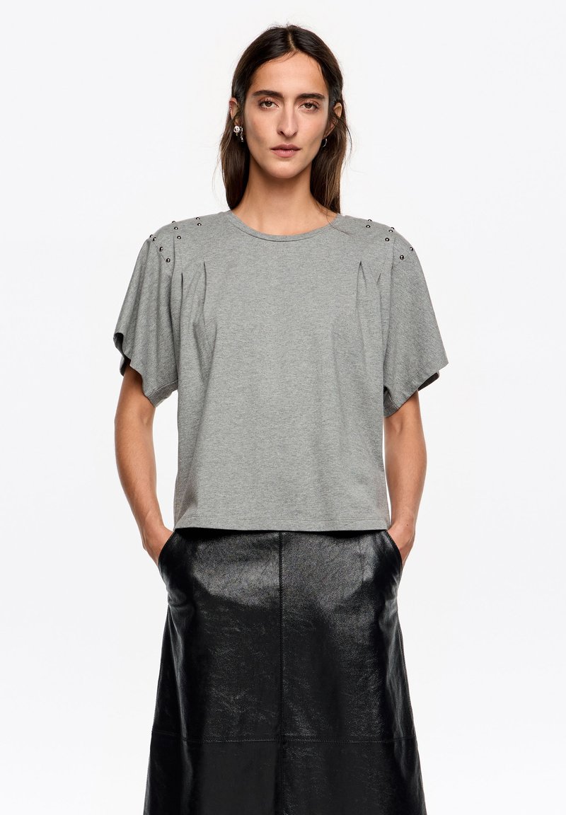 Szara bawełniana koszulka z krótkim rękawem, ozdobiona plisami i metalowymi ćwiekami na ramionach. Połączona z długą czarną skórzaną spódnicą.