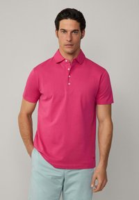 Pánská polokošile s krátkým rukávem v jasně růžové barvě, vyrobená z hladké bavlny. Má límec, zapínání na tři knoflíky a decentní logo na lemu.