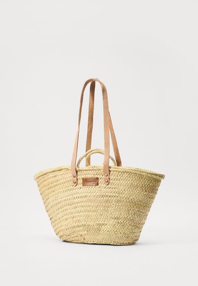 Sac fourre-tout en paille tissée avec des poignées en cuir beige, de forme arrondie et base plate. Il est doté d'une petite étiquette en cuir avec le nom de la marque et des accents métalliques.