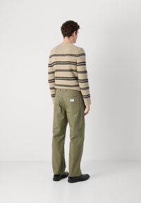 Knit sweater in beige with black stripes paired with green cotton pants. The pants feature back pockets and a label at the center.