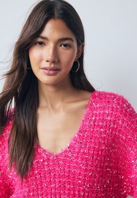 Felroze gebreide trui met een losse pasvorm, V-hals en een gestructureerde afwerking, met metallic accenten door de hele stof.