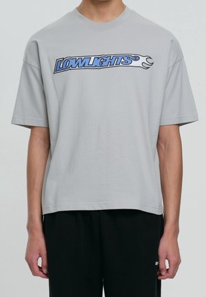 Jasnoszary bawełniany t-shirt z niebiesko-czarnym graficznym logo „LOWLIGHTS” na wysokości klatki piersiowej, z krótkimi rękawami i luźnym krojem.