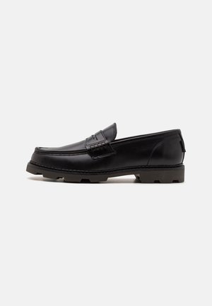 Black leather loafers with a rounded toe, decorative stitching, and a textured outsole for traction. Slightly elevated heel.