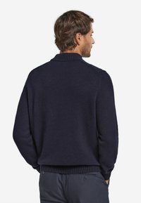 Dunkelblaues Strickpullover mit geripptem Kragen, überschnittenen Schultern und lockerer Passform. Gleiche Textur, keine sichtbaren Muster oder Akzente.