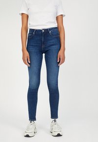 Džíny s vysokým pasem a úzkým střihem v modré barvě vyrobené z denimu, s klasickým zapínáním na knoflík a zdrhovadlo a s jemným vyblednutím podél nohavic.