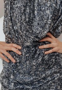 Robe ornée de sequins avec un tissu texturé argent et noir, au design ajusté, présentant une finition scintillante et un détail de taille froncée.