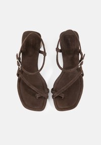 Καφέ σουέντ φλατ σανδάλια με λεπτά λουράκια στον αστράγαλο, θηλιές για τα δάχτυλα, τετράγωνο σχέδιο στο μπροστινό μέρος και μικρή ασημί αγκράφα σε κάθε πλευρά.