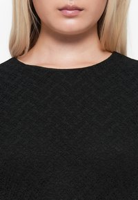 Black textured garment featuring a round neckline and a diamond pattern on the fabric, displaying a soft, matte finish.