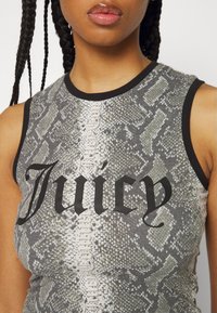 Gros plan d'une personne portant un haut sans manches à motif serpent avec bordure noire et texte en gras « Juicy » sur la poitrine.