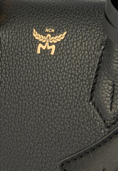 Sac à main en cuir grainé noir avec un logo MCM doré au design ailé et un détail de couture distinctif le long des bords.