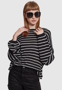 Black and white striped sweater with a loose fit and long sleeves, paired with black shorts and large square sunglasses.