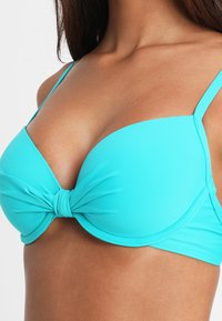 Top de bikini turquesa hecho de material suave y elástico, con un detalle de centro anudado y tirantes finos ajustables.