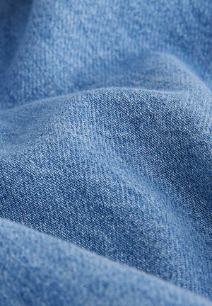 Denimstof i lys blå, der viser en blød, tekstureret overflade med et synligt twill vævemønster. Materialet ser let krøllet ud.