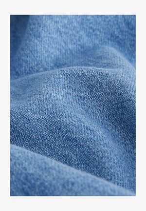 Heledsinine denimkangas, millel on pehme, tekstuurne pind ja nähtav kootud mustrikujundus. Materjal näeb välja kergelt kortsunud.