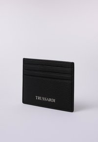 Portafoglio in pelle nera con tre slot per carte, superficie testurizzata e logo "TRUSSARDI" in argento sulla parte anteriore.