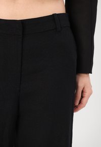 Pantalons en lin noirs avec une taille plate, une taille ajustée et des poches latérales. Le tissu a une finition légèrement texturée et une coupe décontractée.