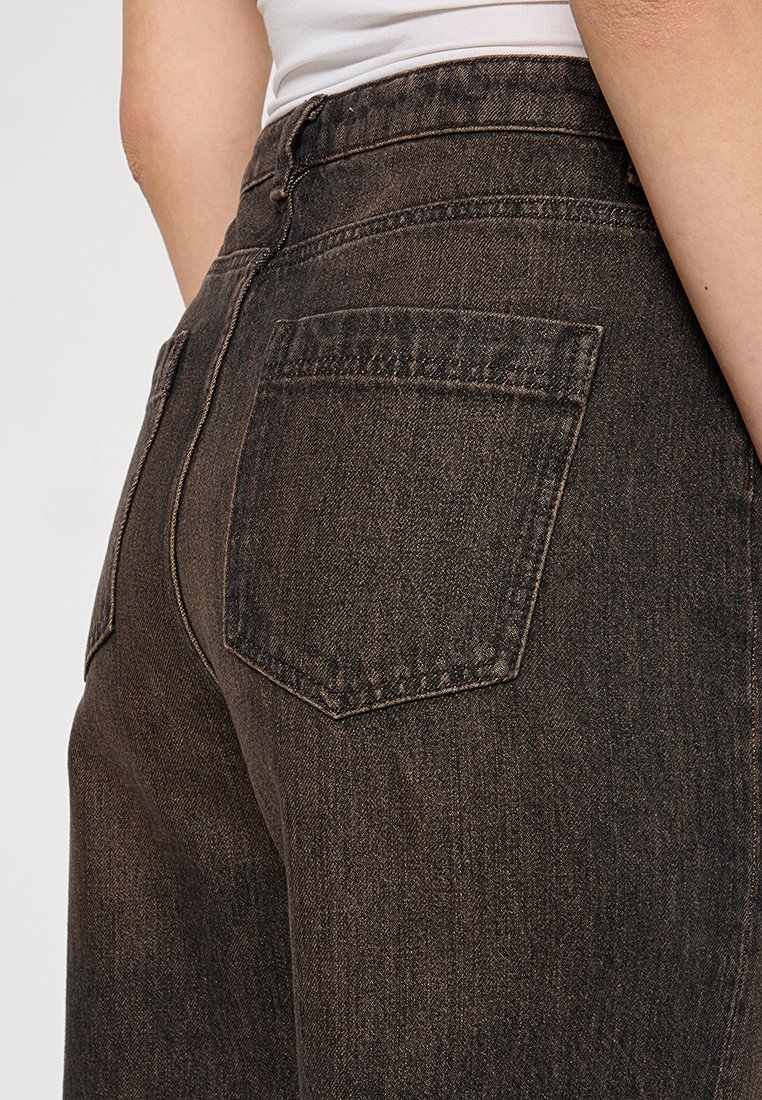 Dunkelbraune Denim-Jeans mit hoher Taille, zwei Gesäßtaschen und einer leicht strukturierten Oberfläche. Die Nähte sind in einem kontrastierenden helleren Faden gehalten.