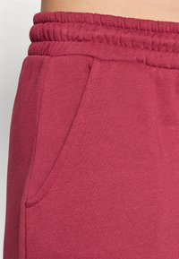 Bordeaux joggebukser har elastisk midje og en sidelomme. Stoffet er mykt og lett med en jevn tekstur.