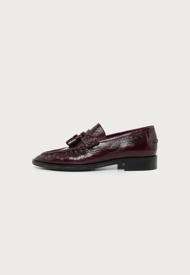 Mocassin en cuir bordeaux foncé brillant avec pompons, talon noir bas et coutures détaillées le long du bord supérieur, présenté de profil.