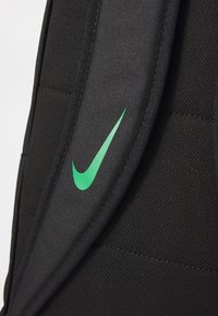 Zaino in tessuto nero con un grande logo verde Nike swoosh, dotato di spallacci imbottiti e dettagli di superficie testurizzati.