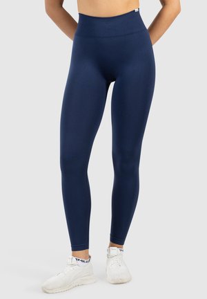 Marineblauwe high-waisted leggings van rekbaar materiaal. Glad textuur, figuurvormend ontwerp en enkellang met een geribde tailleband.